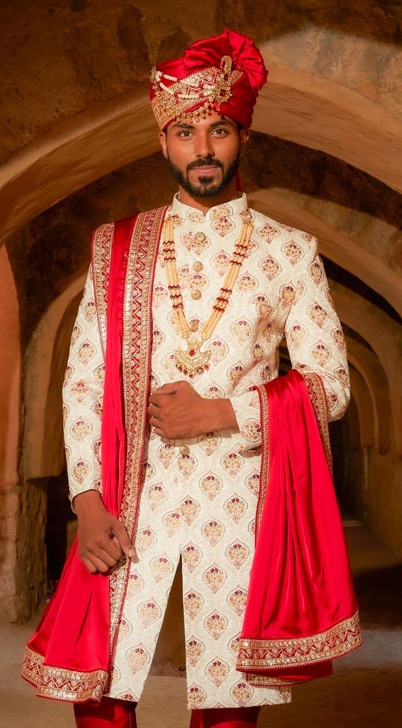 Man in an ivory embroidered wedding kurta set with a red stole