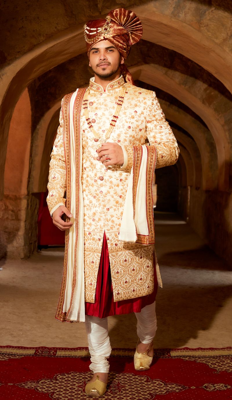 Groom in an ivory embroidered kurta set walking through arches