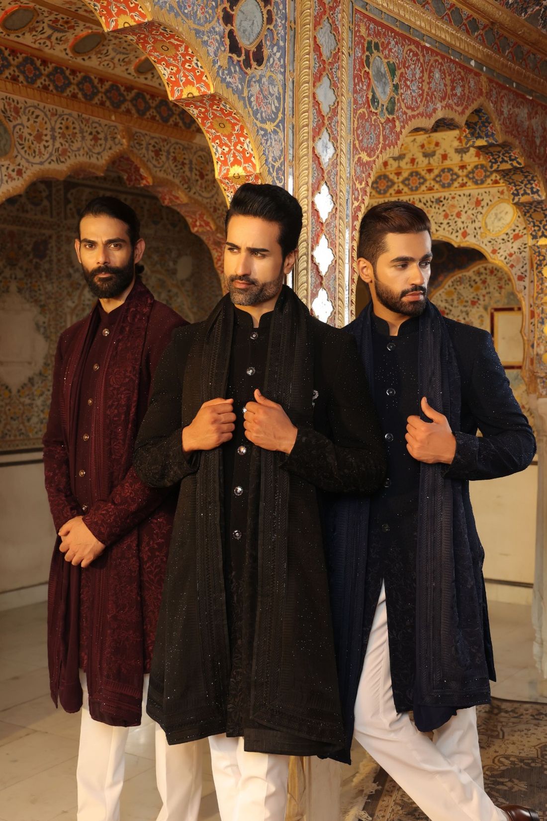 Three men in embroidered dark kurta sets in an ornate hall